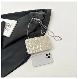 Detail of metallic clutch featuring embossed letter pattern with a silver chain strap