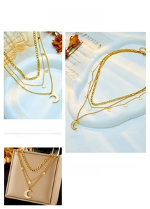 Detail of layered gold necklace with moon and star pendants on a textured tray
