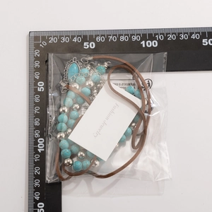 Detailed view of bohemian beaded necklace with turquoise stones in packaging beside scale