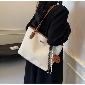 Detail of canvas tote bag with brown leather handles and a teddy bear charm