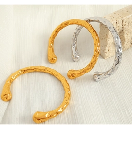 Close-up of hammered gold and silver open bangles on elegant satin and stone background