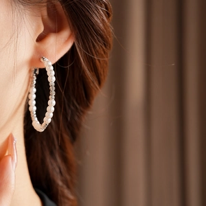 Close-up of a large hoop earring with small white pearls and textured silver beads