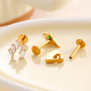 F136 titanium gold earring set with green and clear zircon crystals on beige plate