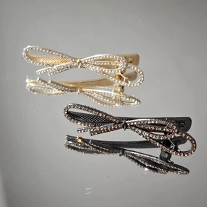 Fashionable bow hair clips with rhinestones in gold and black finish on mirrored surface