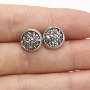 Macro shot of 8mm silver stainless steel stud earrings held on a finger for size scale