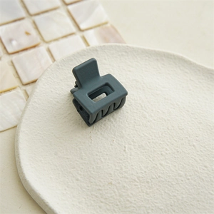 Detailed view of a small matte grey-green square hair claw clip on a beige ceramic plate