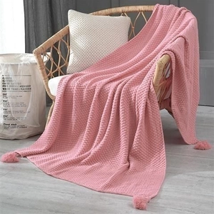 Detail of pink waffle knit throw blanket with decorative tassels on a rattan chair