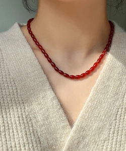 Detail of elegant red agate beaded necklace worn on neck over a soft knit sweater