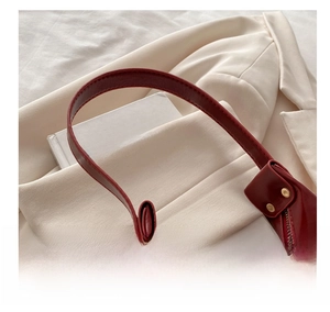Detail of red crescent bag handle with gold rivets on a cream blazer and book