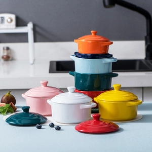 Mini ceramic ramekins with lids and handles in various colors on a blue kitchen counter
