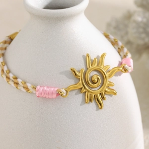 Bracelet tressé avec pendentif soleil doré 18K et cordon rose et beige sur support blanc