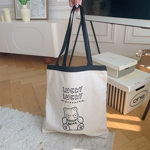 Detail of canvas tote bag featuring lucky bear embroidery and black woven handles