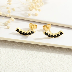 Macro shot of 18K gold plated studs with curved black zircon stones on white floral background
