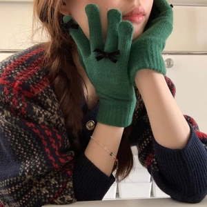 Close-up of green knitted winter gloves featuring a decorative black bow detail