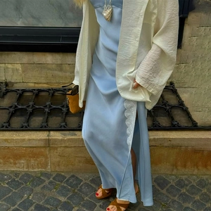 Hellblaues Seiden-Maxikleid mit Spitze und weißem Cardigan auf einer Pflasterstraße