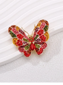 Close-up of golden butterfly brooch featuring multicolored crystals and red teardrop stone