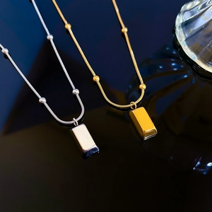 Macro detail of gold and silver minimalist brick necklaces with beaded snake chains