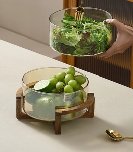 Detail view of a glass salad bowl set with solid wood cross stand and vibrant fruits
