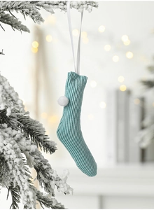 Close-up of a light blue knitted mini Christmas stocking with a white pompom and ribbon