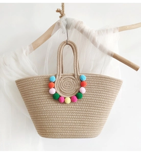 Detail of straw woven tote bag featuring colorful pom-poms on a rustic background