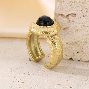 Bague texturée dorée avec pierre noire sur fond de pierre beige et soie douce
