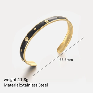 Close-up of gold-plated stainless steel C-shape cuff with black enamel and star details