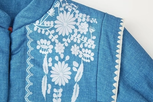 Dettaglio della giacca di jeans blu con ricamo floreale bianco e bordo ondulato