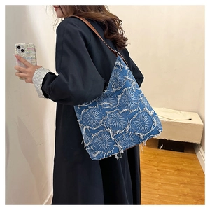 Detail of blue washed denim tote bag featuring white fringe floral textures and brown strap