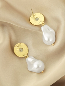 Detailed view of long baroque pearl drop earrings on light gold satin background