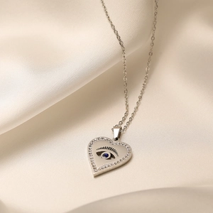 Silver heart necklace with evil eye pendant and blue zircon on white silk background