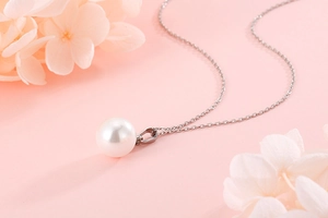 Detail of silver chain necklace featuring a white pearl pendant on a soft pink floral background