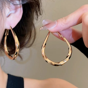 Macro shot of large golden twisted hoop earrings featuring a polished mirror finish