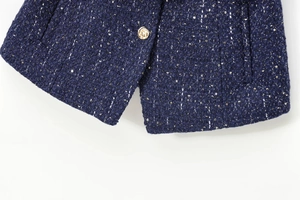 Detail of navy tweed fabric with shimmering sequins and an elegant gold embossed button