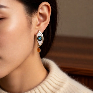 Close-up of vintage eye-shaped earring with blue gem and amber teardrop on a model