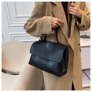 Detail of black crocodile texture handbag with adjustable strap shown on model in trench coat