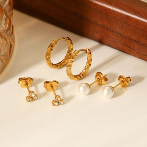 Detailed set of hammered gold hoops, zircon studs, and pearl earrings on a white surface