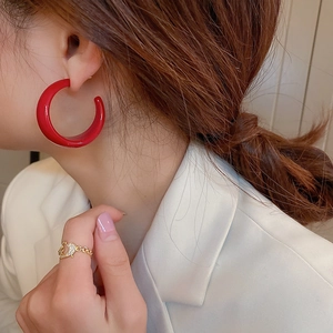 Close-up of red C-shaped hoop earring on model with golden heart chain ring detail