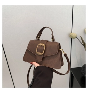 Detail of a brown faux leather handbag featuring a vintage gold ring buckle and top handle