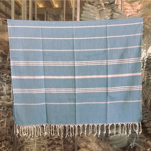 Detailed texture of light blue striped Turkish towel featuring handmade white fringe tassels