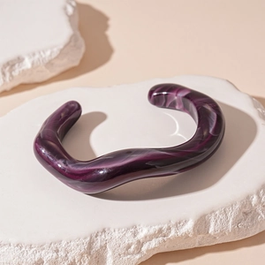 Macro shot of wavy irregular purple marble resin cuff bracelet on stone base