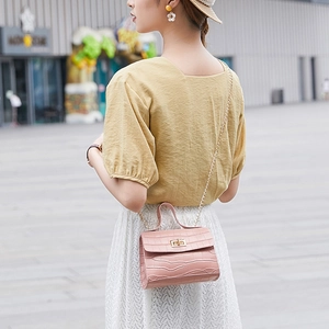 Pink crocodile pattern handbag with gold chain strap shown in an outdoor street setting