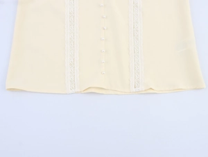 Detailed close-up of beige blouse hem with white lace trim and pearl buttons