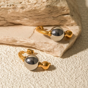 Gros plan de boucles d'oreilles en acier inoxydable bicolore sur socle en pierre