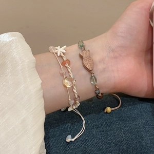 Detail eines gewebten Armbands mit Holzfisch, Seestern und Natursteinen