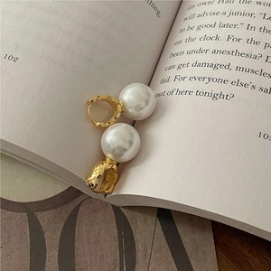 Detailed view of quilted gold earrings with white pearls placed on an open book