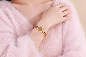 Detail of gold Tree of Life bracelet with pavé cubic zirconia on model wearing pink sweater