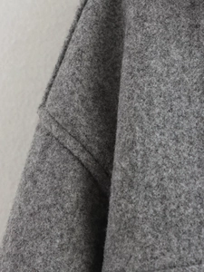 Dettaglio macro della trama in lana grigio scuro e cuciture del cappotto con risvolto