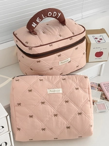 Detail of pink quilted cosmetic bag set featuring brown bow embroidery and a top handle