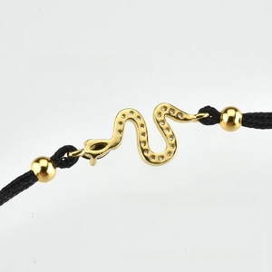 Detailed view of a gold snake pendant with zircon pavé on a black woven cord bracelet