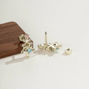 Boucles d'oreilles sapin de Noël dorées avec zircons colorés et perles sur fond beige